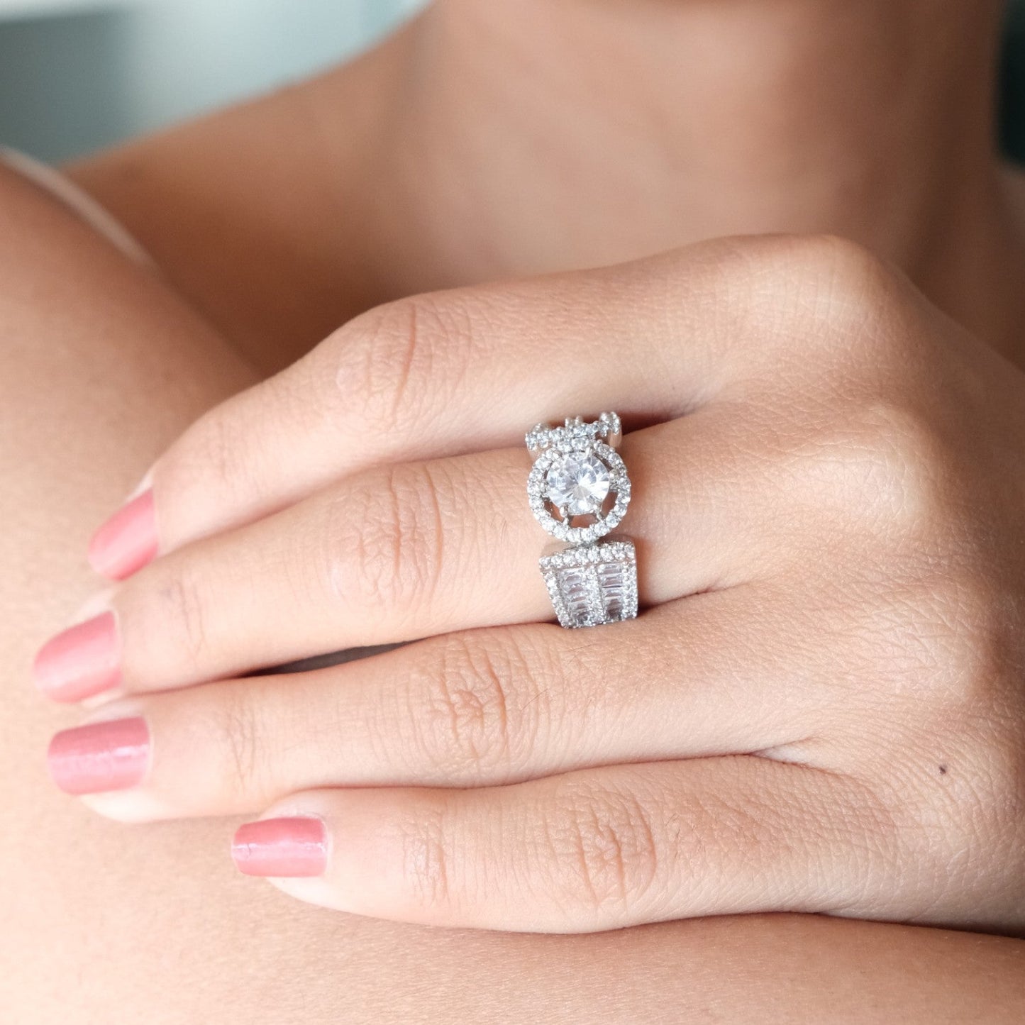 A close-up lifestyle shot of a woman wearing a silver-toned ring with a round-cut center stone and pavĂŠ-set side stones on her ring finger.
