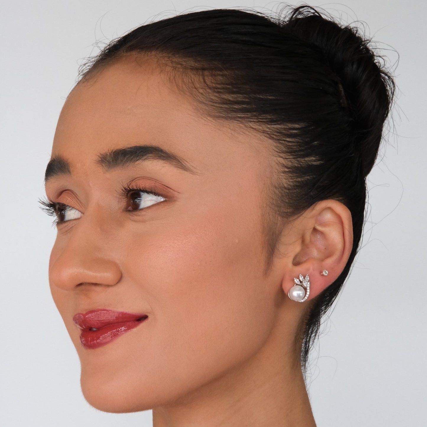 Woman with a side bun wearing earrings against a plain background