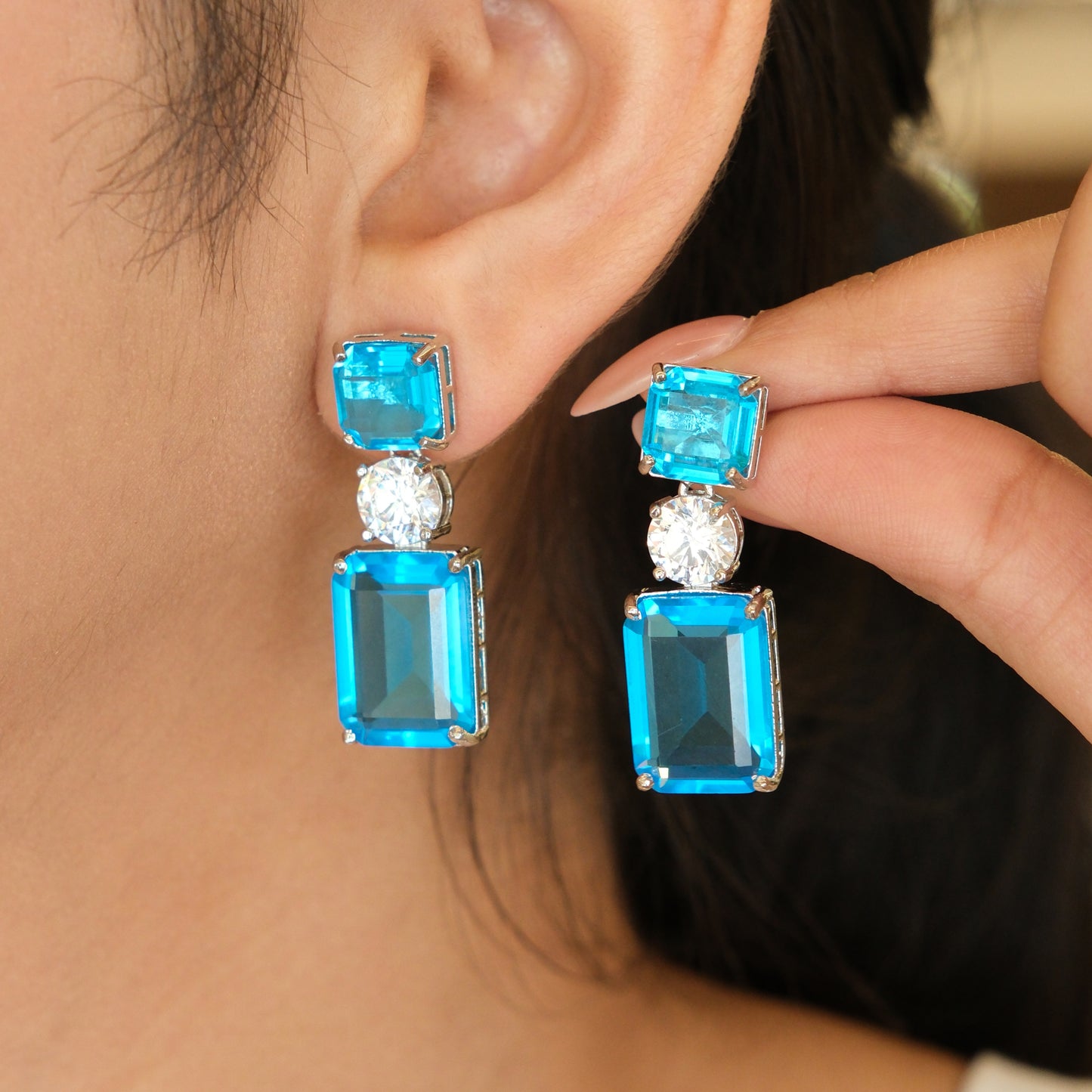 Model wearing blue gemstone drop earrings with crystal accents in a lifestyle portrait