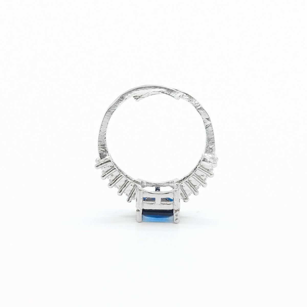 A silver ring featuring a textured band, a row of small clear stones, and a central rectangular blue gemstone, shown on a plain white background.