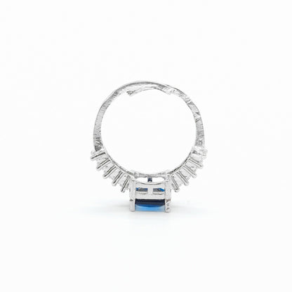A silver ring featuring a textured band, a row of small clear stones, and a central rectangular blue gemstone, shown on a plain white background.