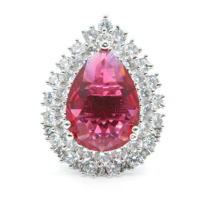 A teardrop-shaped halo ring featuring a large faceted pink gemstone in the center, surrounded by a double halo of small clear stones in a silver-toned setting, isolated on a white background.