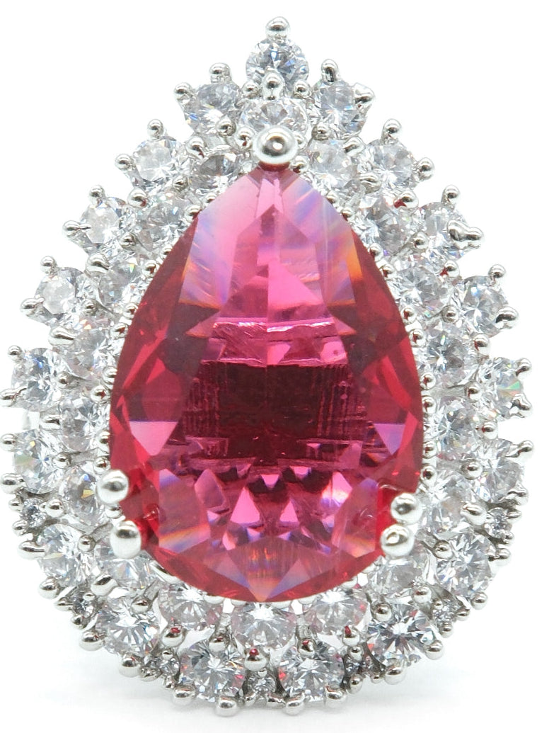 A teardrop-shaped pink gemstone halo ring set in silver-toned metal with surrounding clear stones, photographed on a plain white background.