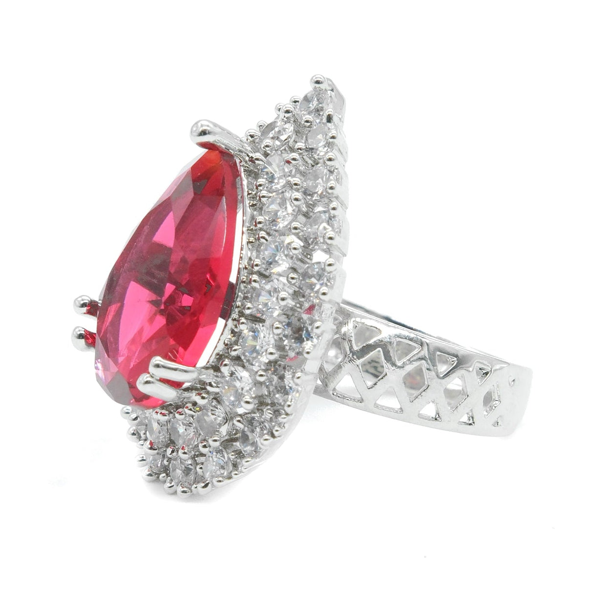 A silver ring featuring a large teardrop-shaped red gemstone surrounded by a halo of small clear stones, with a textured silver band, shown on a plain white background.