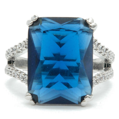 A rectangular blue gemstone ring with a silver-toned setting and pavé diamond accents on the band, shown against a plain white background.