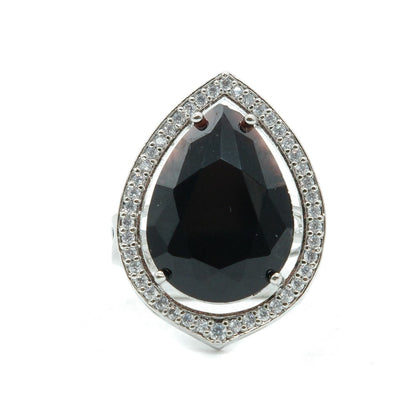 A teardrop-shaped ring featuring a large black gemstone in a silver-toned halo setting with small clear stones around the perimeter, shown on a plain white background.