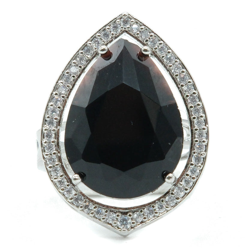 A teardrop-shaped silver ring featuring a large faceted black onyx center stone surrounded by a halo of small clear pavé stones, set against a plain white background.
