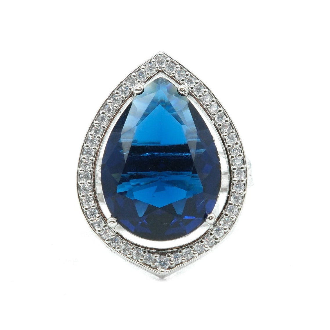 A teardrop-shaped blue gemstone ring with a silver-colored halo setting accented by small clear stones, shown on a plain white background.