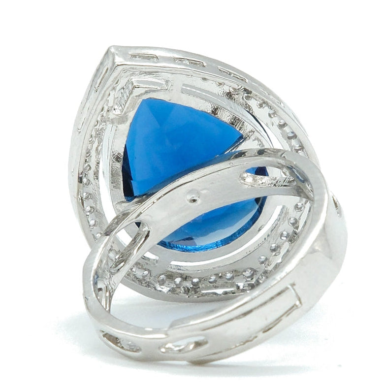 A silver ring featuring a large, teardrop-shaped blue gemstone surrounded by a halo of small clear stones, set on a plain white background.