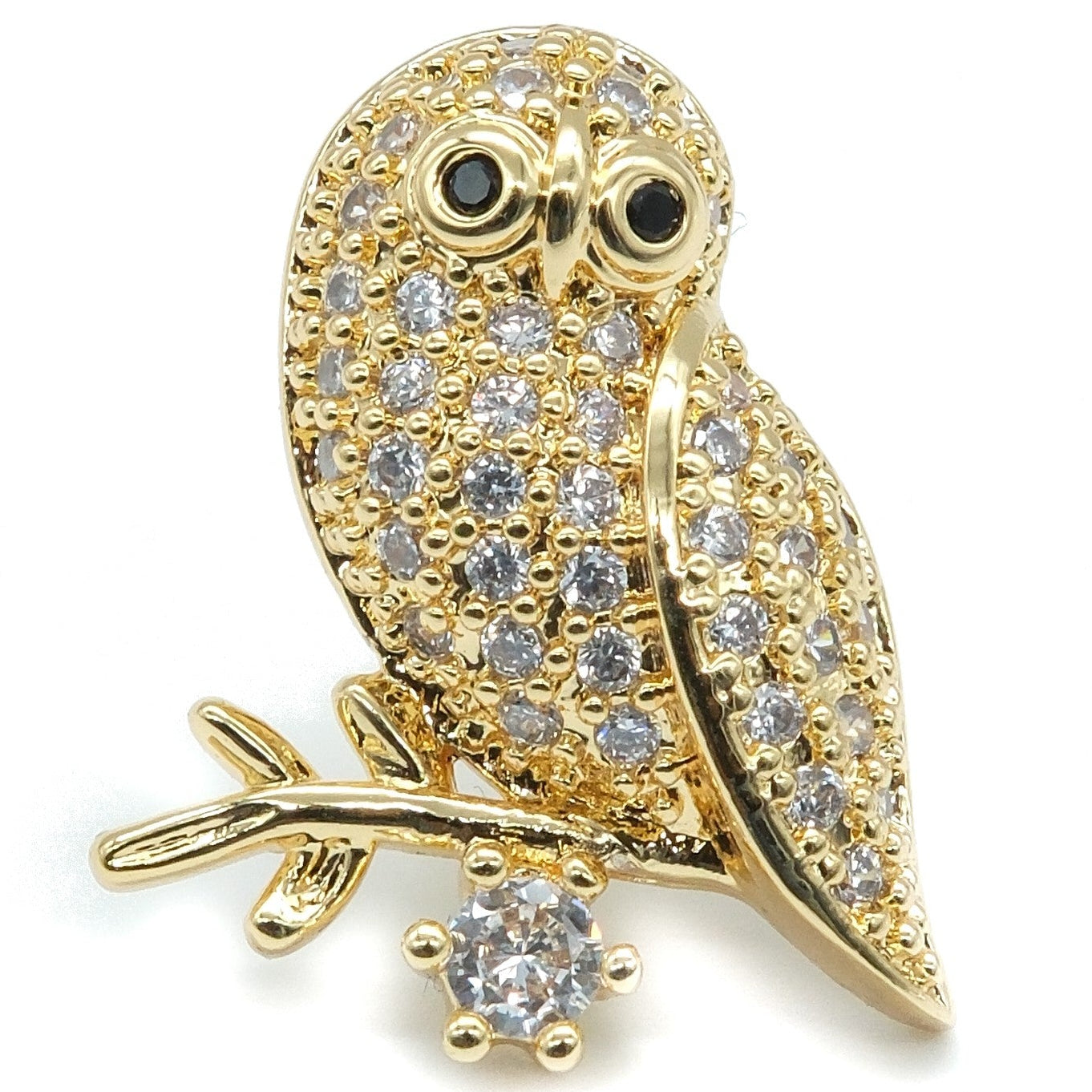 Gold owl brooch embellished with clear pavé stones and small black stone eyes, perched on a branch with a dangling clear stone, shown on a white background.