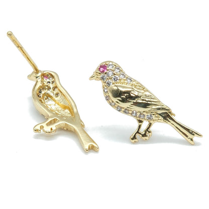 A pair of gold bird stud earrings on a plain white background. One earring features a bird perched on a branch with a small pink gemstone accent, while the other is a standing bird embellished with clear rhinestones and a pink gemstone on its head.