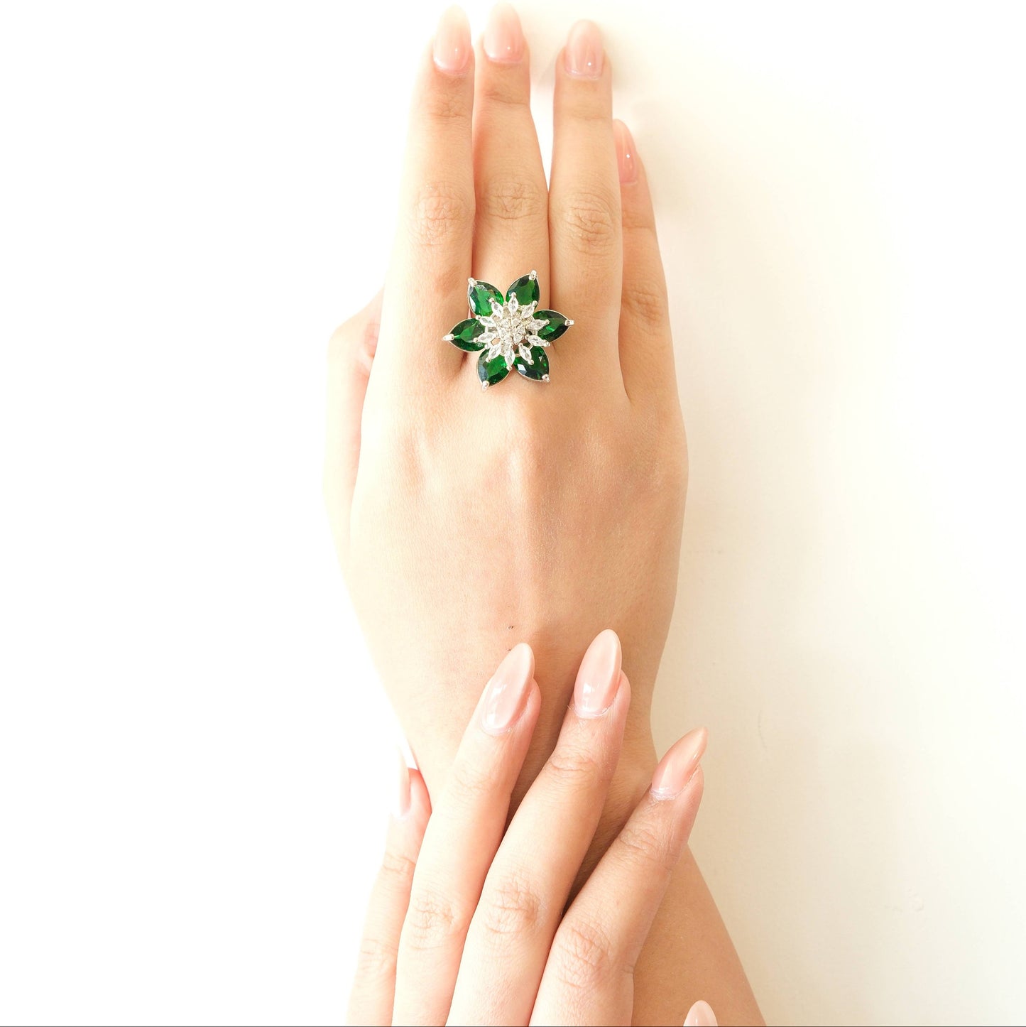 A hand wearing a green and silver flower-shaped ring, photographed against a clean white background.