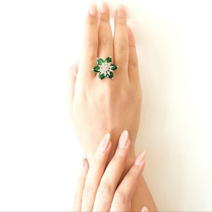 A hand wearing a green and silver flower-shaped ring, photographed against a clean white background.