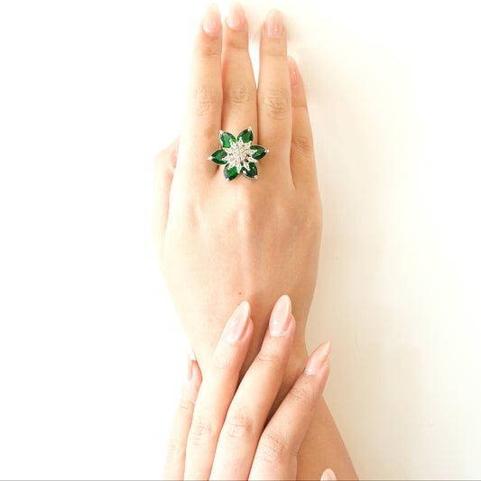 A hand wearing a green and silver flower-shaped ring, photographed against a clean white background.