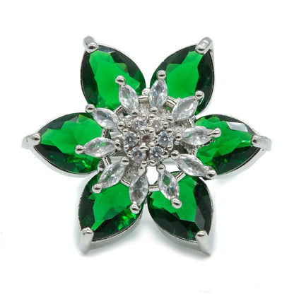 A silver-tone flower-shaped brooch featuring six green marquise-cut stones and a clear crystal center, shown on a plain white background.