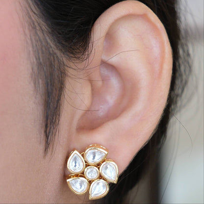 A close-up of a person's ear wearing a gold flower-shaped stud earring with white teardrop-shaped stones.