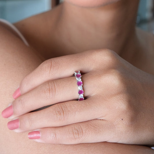 A close-up of a woman's hand wearing a slim silver band ring set with alternating pink and clear gemstones, shown against her shoulder.