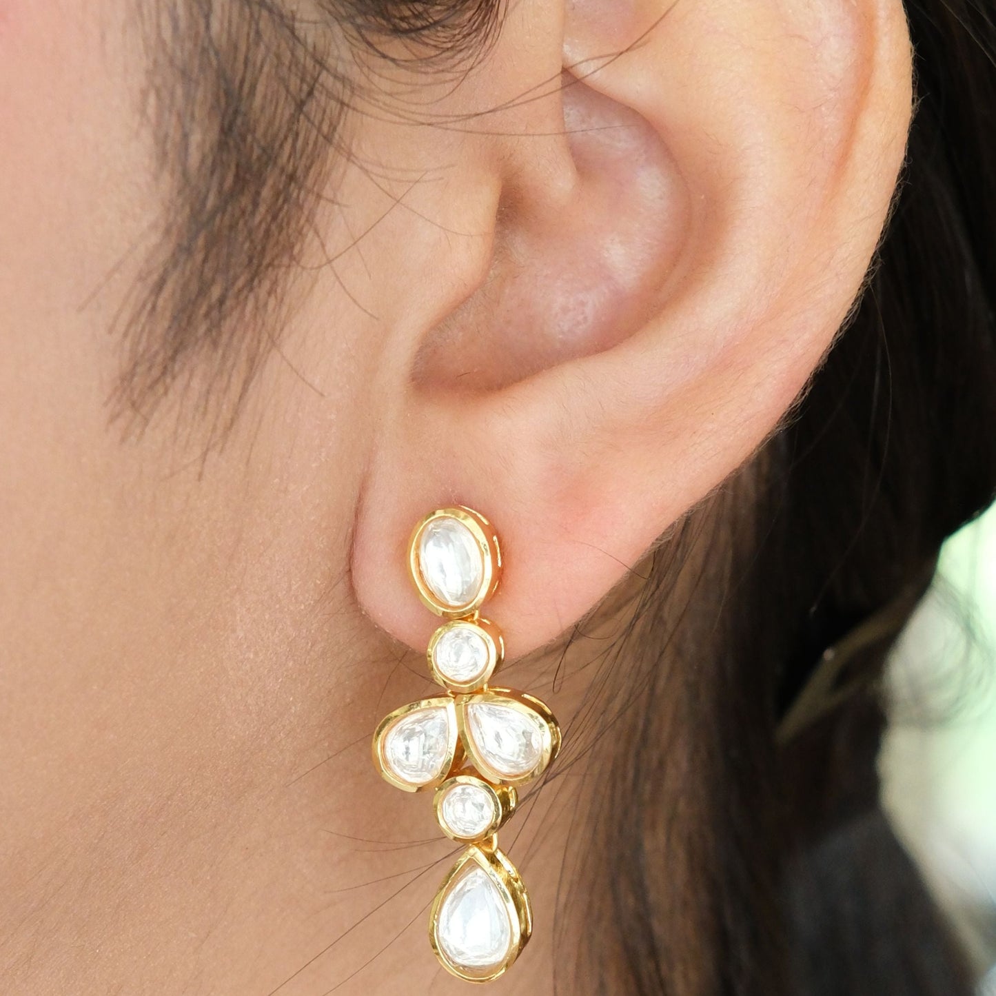 A close-up of a person's ear wearing a gold drop earring with white pearl-like stones.