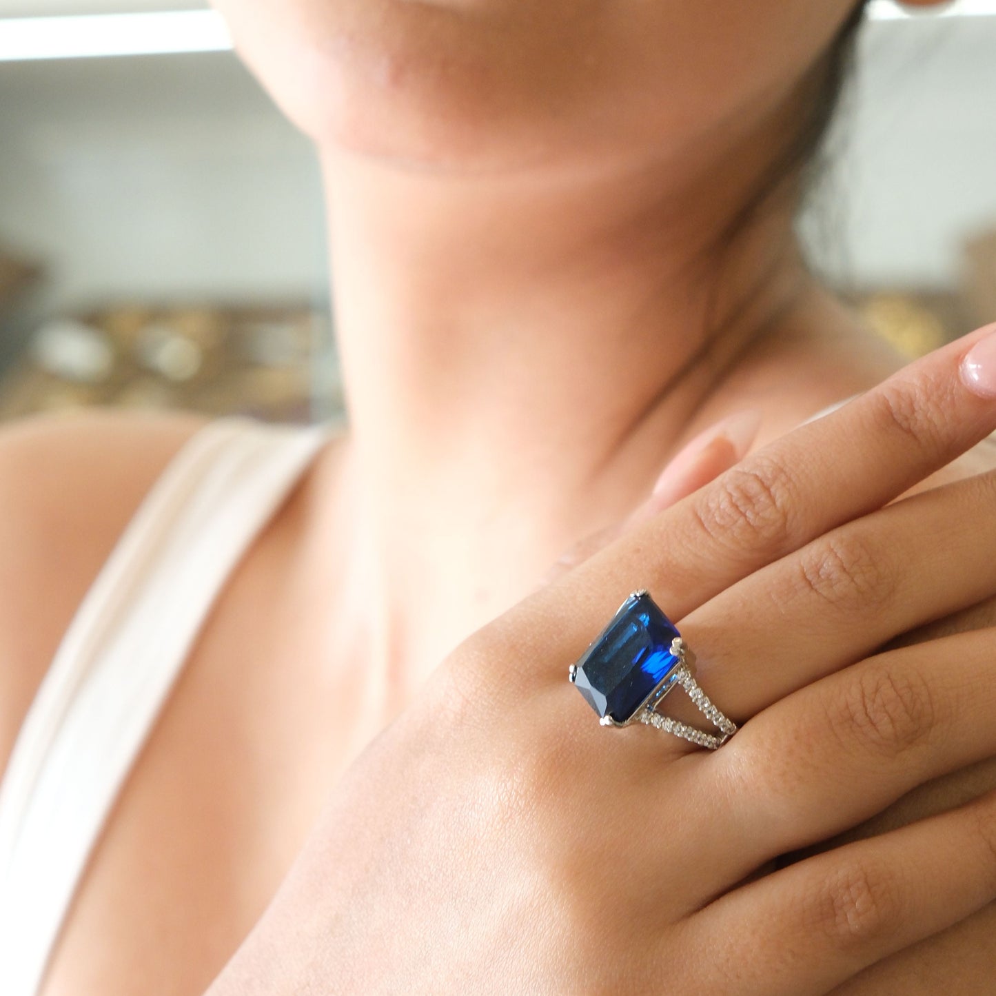 A close-up lifestyle shot of a woman wearing a silver ring with a rectangular blue gemstone on her finger.