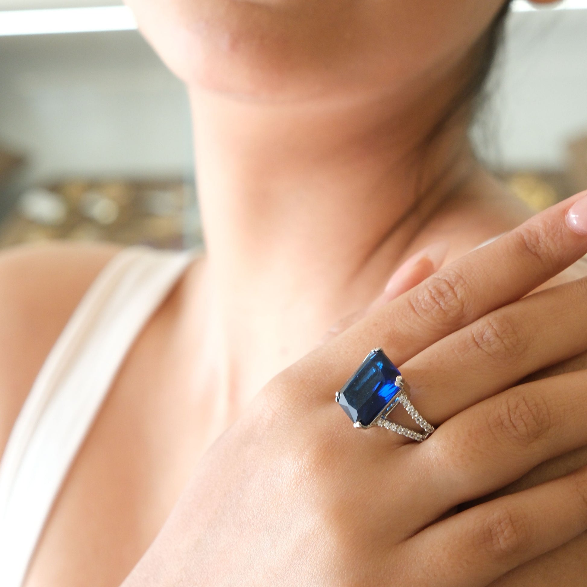 A close-up lifestyle shot of a woman wearing a silver ring with a rectangular blue gemstone on her finger.