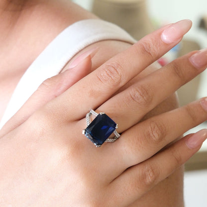 A close-up of a person's hand wearing a silver ring with a large rectangular dark blue gemstone.