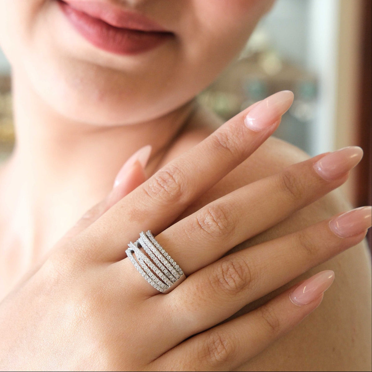 A close-up lifestyle shot of a woman wearing a silver-toned multi-band ring with small clear stones, shown on her finger with her hand resting on her shoulder.