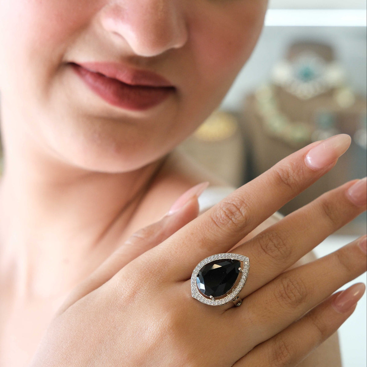 A close-up lifestyle shot of a woman wearing a large teardrop-shaped black gemstone ring with a halo of small clear stones on her finger.