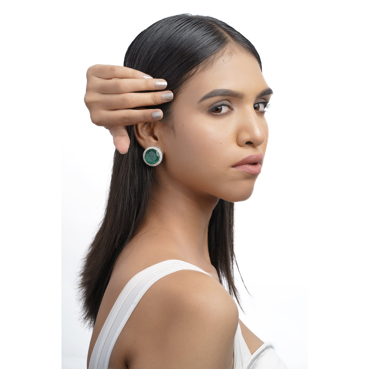 Model posing in white outfit wearing emerald green statement earrings