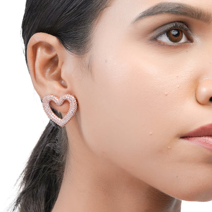 Model wearing rose-tone heart earring with pink sparkle stones